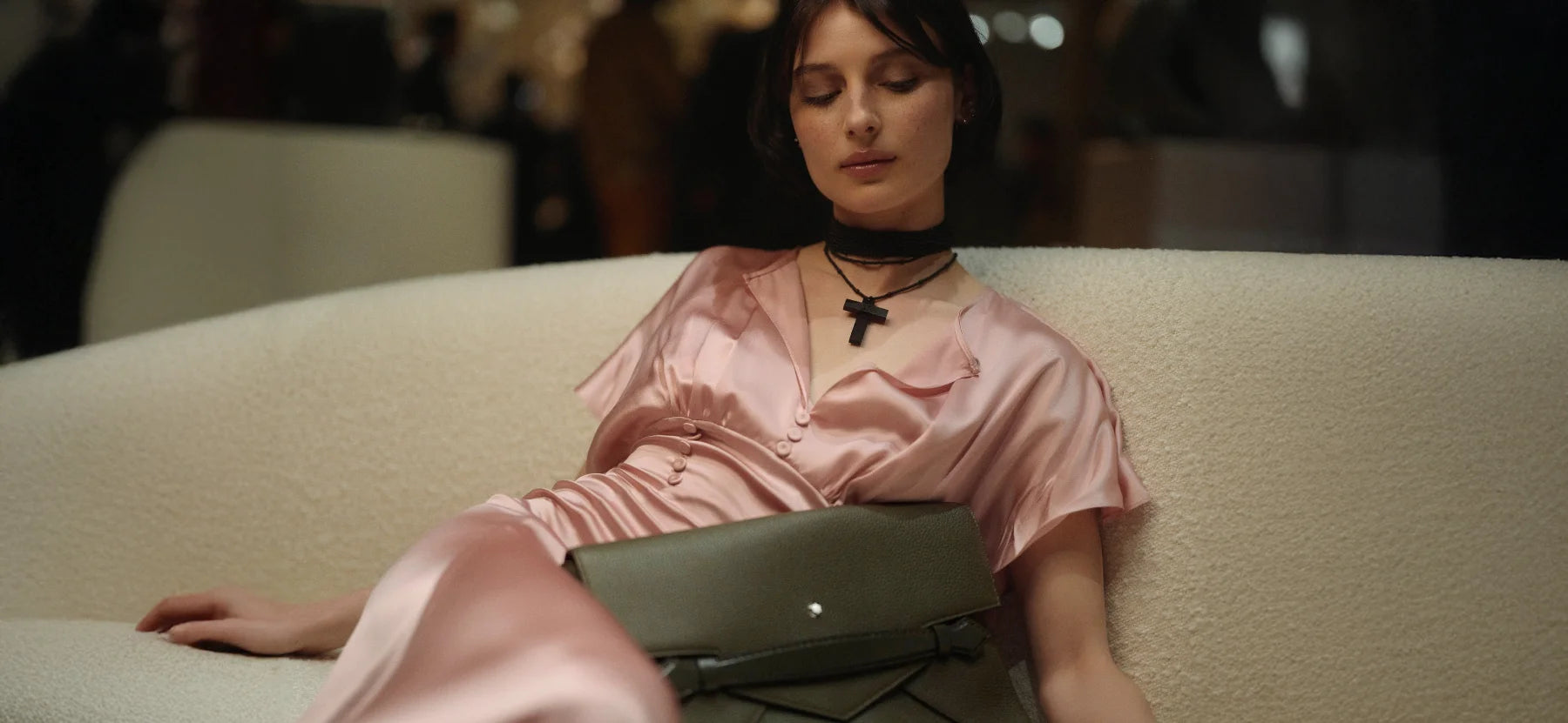 Nahaufnahme einer eleganten Frau in einer rosa Satinbluse, die eine olivgrüne Montblanc Envelope Clutch präsentiert. Die Tasche mit ihrem markanten Umschlag-Design ist jetzt erhältlich im juwelier-tirol.shop.